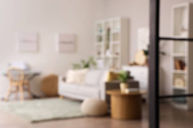 Gri kanepe, sehpa ve raf üniteleriyle aydınlık oturma odasının bulanık görüntüsü