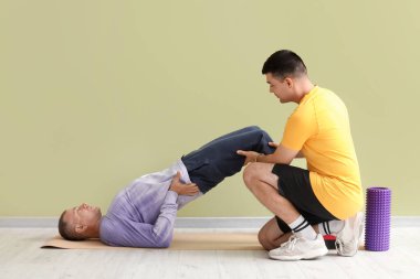 Yeşil duvarın yanında rehabilitasyon terapistiyle paspasın üzerinde yetişkin adam eğitimi.
