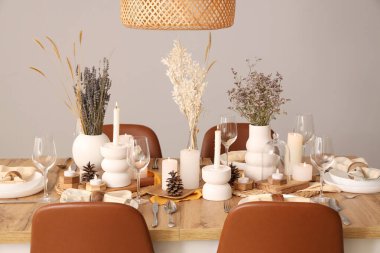 Kurumuş çiçekleri, yanan mumları ve kozalakları olan zarif bir masa.