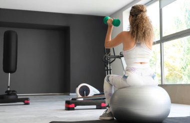 Yetişkin bir kadın spor salonunda spor salonunda halterlerle egzersiz yapıyor.