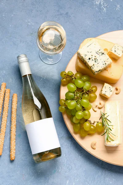 Tasty cheese, grapes, grissini, bottle and glass of wine on blue background