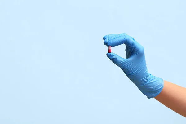 Hand of doctor in glove with pill on blue background