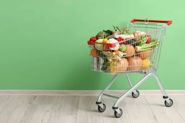 Shopping cart full of food near green wall