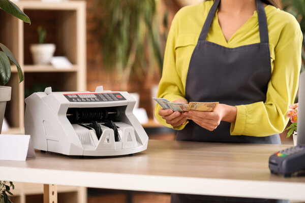 Female cashier with money and cash counting machine in flower shop, closeup
