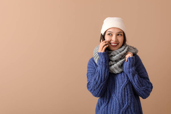 Красивая молодая азиатка в теплом шарфе разговаривает по мобильному телефону на коричневом фоне