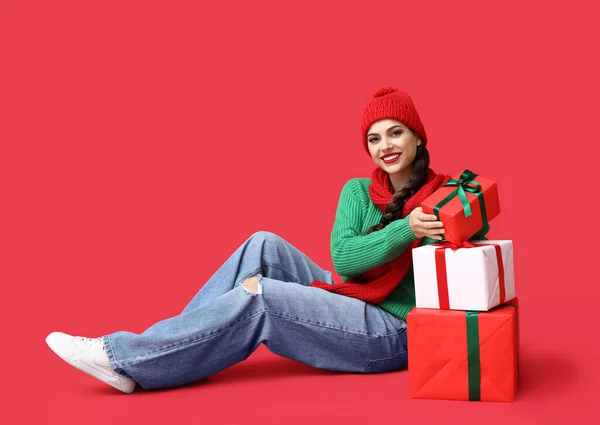 赤い背景にクリスマスの贈り物を持つ美しい若い女性 — ストック写真