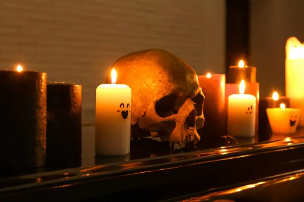 Burning candles and skull for Halloween celebration on grand piano in dark room, closeup