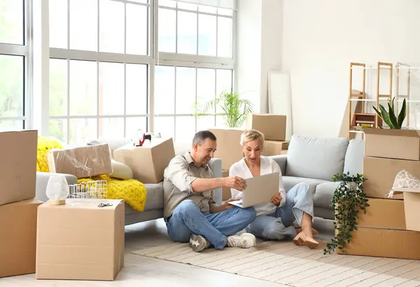 Taşınırken odada dizüstü bilgisayar kullanan yetişkin bir çift.