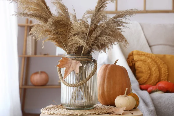 Vase with pampas grass, autumn leaves and pumpkins on table in living room, closeup
