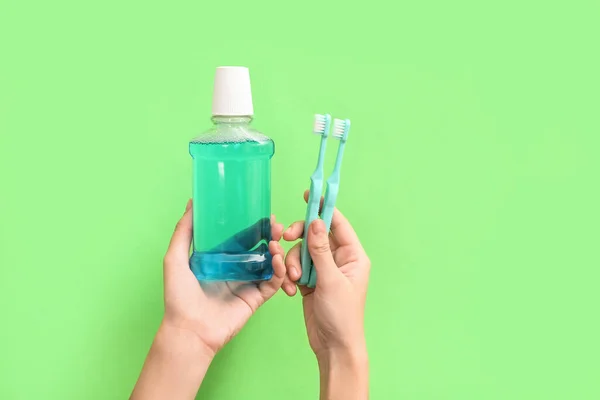 Female hands with mouth rinse and toothbrushes on green background.