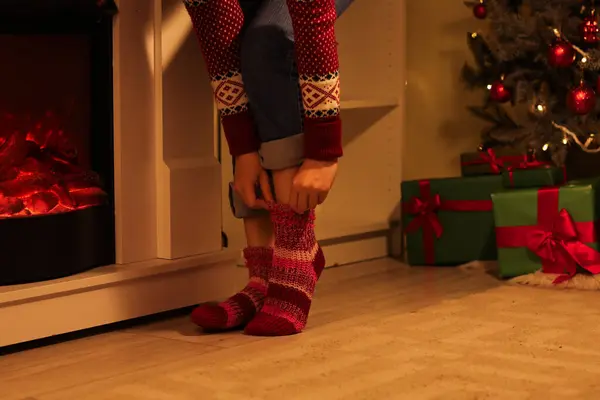 Woman in warm knitted socks near fireplace at home on Christmas eve