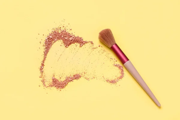 Makeup brush and scattered highlighter on yellow background