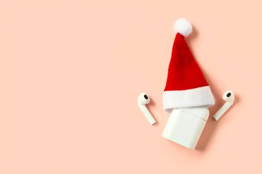 Şarj çantalı modern kulaklıklar ve pembe arka planda Noel Baba şapkası.