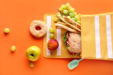 Beslenme çantasında turuncu arka planda farklı lezzetli yiyecekler var.