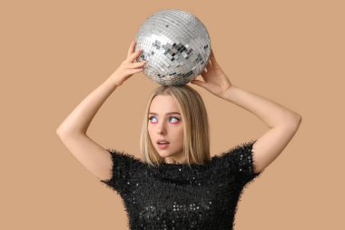 Kahverengi arka planda disko topu olan güzel, düşünceli genç bir kadın.