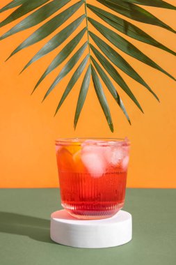 Bir bardak nefis Negroni kokteyli. Arka planda buz küpleri ve palmiye yaprağı var.