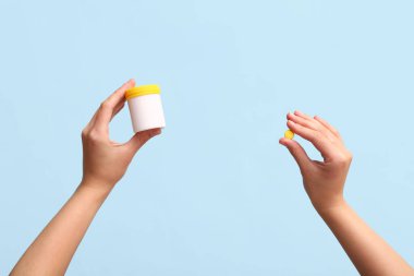 Mavi arka planda ilaç şişesi tutan kadın eller.