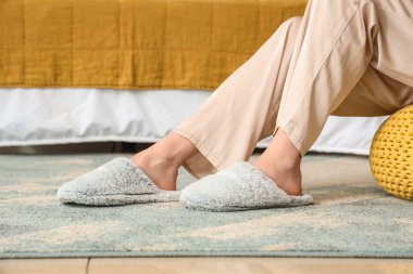 Yatak odasında dinlenen yumuşak terlikli genç bir kadın.