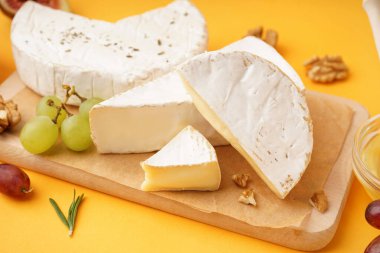 Sarı arka planda lezzetli Camembert peyniri parçaları olan ahşap tahta.