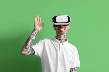 VR kulaklıklı mutlu genç adam yeşil arka planda el sallıyor.