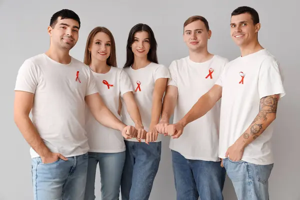 Kırmızı kurdeleli bir grup genç gri arka planda el ele tutuşuyor. Dünya AIDS Günü konsepti