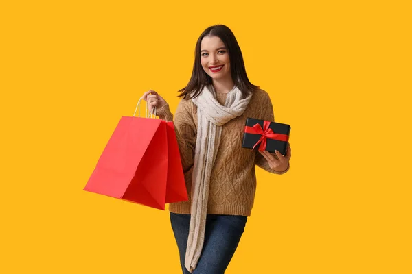 黄色の背景にショッピングバッグとギフトボックスを持っている若い女性 — ストック写真