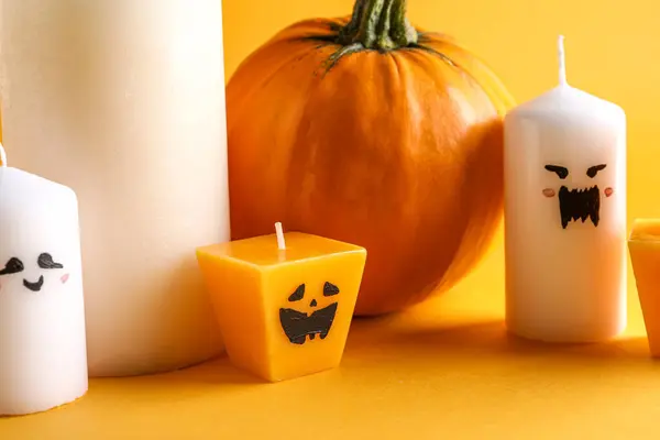 Wax candles and pumpkin for Halloween on yellow background