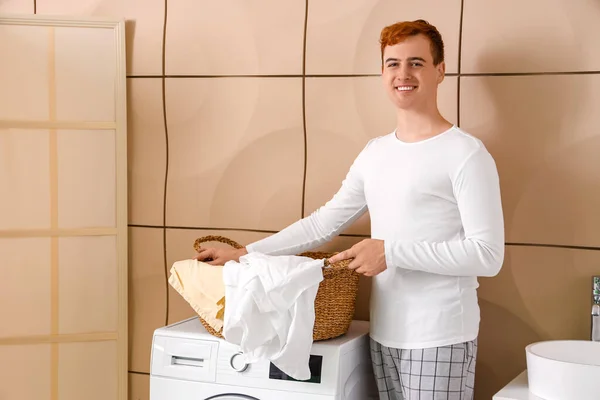 Young man with laundry basket near washing machine