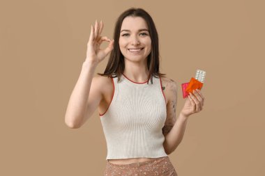 Doğum kontrol hapları ve prezervatifleri olan güzel bir genç kadın kahverengi arka planda iyi bir jest gösteriyor. AID farkındalık kavramı