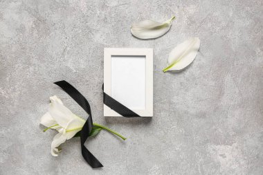 Gri grunge arkaplanda siyah kurdeleli ve zambak çiçekli boş fotoğraf çerçevesi
