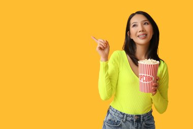 Sarı arka plandaki bir şeyi işaret eden patlamış mısırlı genç Asyalı kadın.