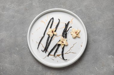 Aromatik vanilyalı tabaklar ve gri arka planda çiçekler.