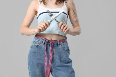 Çatal bıçakları ve gri arka planda şeritleri olan genç ve güzel bir bayan. Kilo verme konsepti