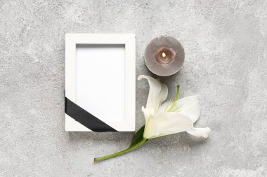 Siyah kurdeleli boş fotoğraf çerçevesi, gri grunge arka planda mum ve zambak çiçeği.