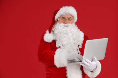Kırmızı arka planda dizüstü bilgisayar kullanan Noel Baba
