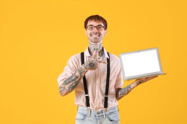 Mutlu genç adam sarı zemin üzerinde modern dizüstü bilgisayarın boş ekranını işaret ediyor.