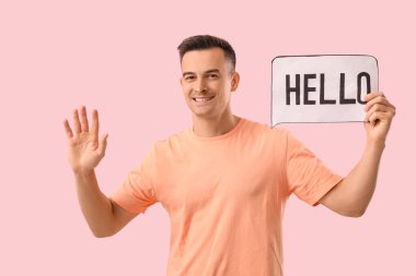 Elinde pembe arka planda kelime merhabası olan kağıt konuşma balonu tutan yakışıklı adam.