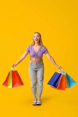 Sarı arka planda alışveriş torbaları olan genç bir kadın.