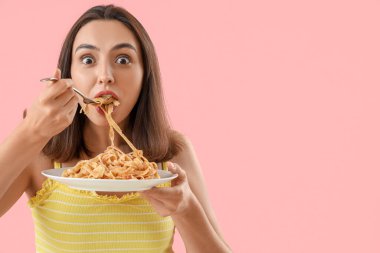 Genç bir kadın pembe arka planda lezzetli makarna yiyor, yakın plan.