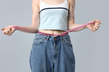 Gri arka planda mezurası olan genç ve güzel bir bayan. Kilo verme konsepti