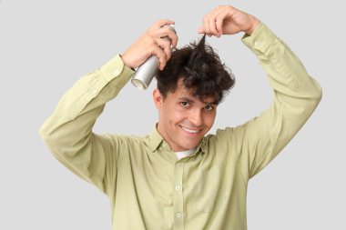 Kıvırcık saçlarına gri arka planda saç spreyi sıkan yakışıklı bir genç.