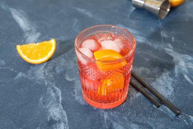 Bir bardak soğuk Negroni kokteyli ve renkli arka planda pipetler.