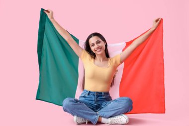 Pembe arka planda oturan Meksika bayrağı taşıyan genç bir kadın.