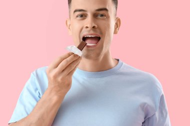 Pembe arka planda çikolata yiyen yakışıklı adam, yakın plan.