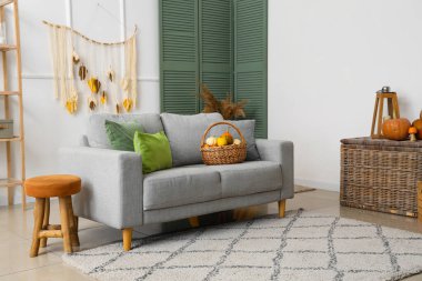 Gri kanepeli, sonbahar yapraklı ve sepetli balkabaklı oturma odasının içi.