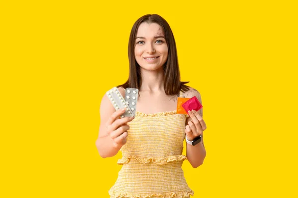 Krásná Mladá Žena Antikoncepčními Pilulkami Kondomy Žlutém Pozadí Koncepce Povědomí — Stock fotografie