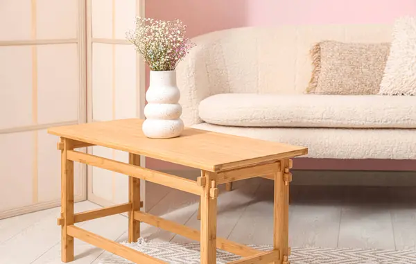 Light wooden coffee table with sofa and dressing screen near pink wall