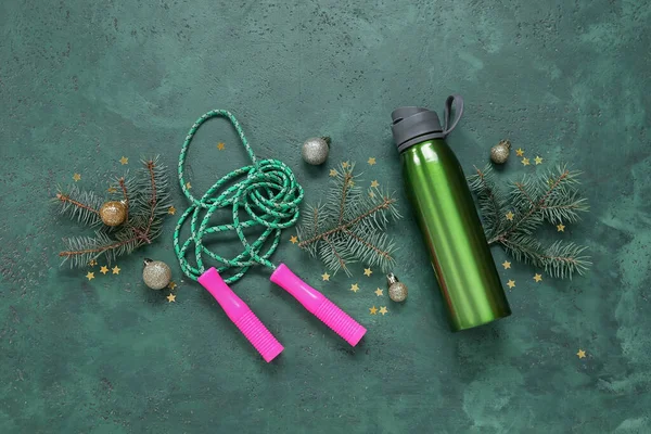 Composition with skipping rope, sports bottle and Christmas tree branches on green background