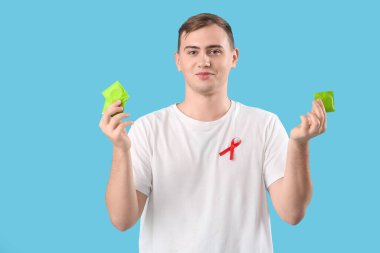 Kırmızı kurdeleli ve mavi arka planda prezervatifli yakışıklı bir genç. Dünya AIDS Günü konsepti