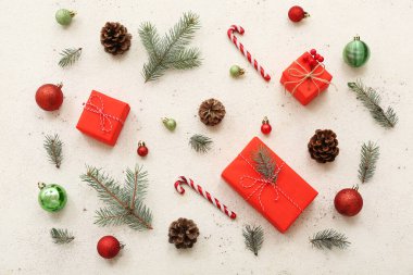 Köknar dalları, koniler, baston şekerler ve beyaz arka planda Noel topları olan hediye kutuları.